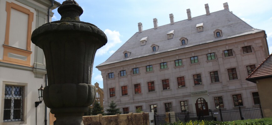 Zdjęcie frontu biblioteki wraz z kamienną rzeźbą stojącą na pagórku przed biblioteką.