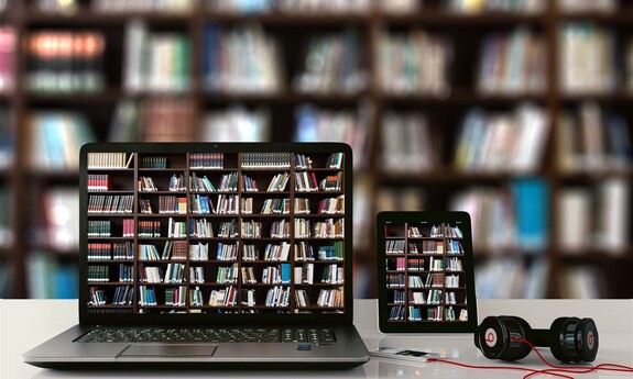 Na zdjęciu jest laptop i czytnik, na ekranie których wyświetlone są półki z książkami., oraz słuchawki.