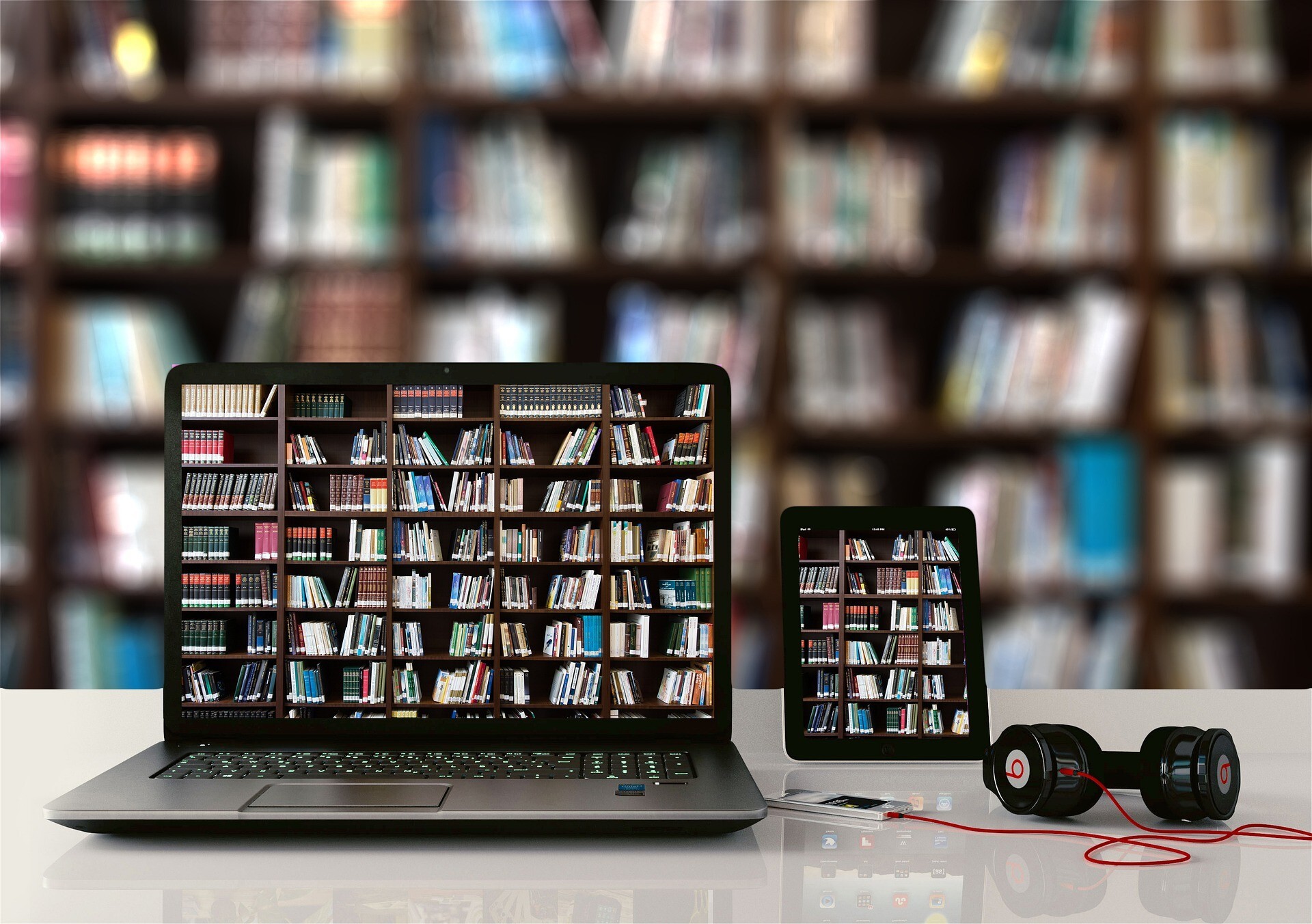 Na zdjęciu jest laptop i czytnik, na ekranie których wyświetlone są półki z książkami., oraz słuchawki.